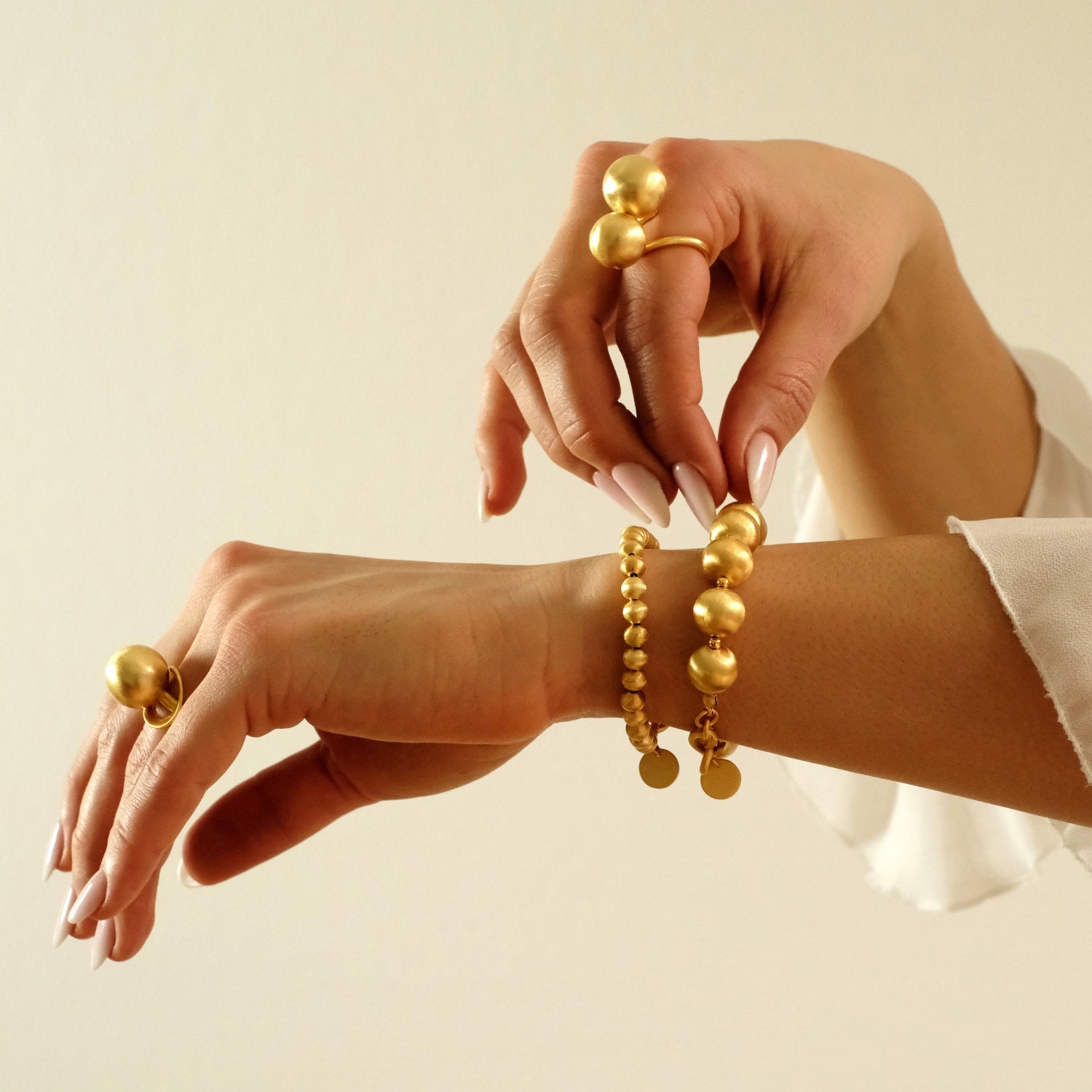 Nahaufnahme von Haenden, die goldene Armbänder und Ringe von Cosytas präsentieren, vor einem minimalistischen, hellen Hintergrund. Eleganz und hochwertiges Design im Fokus.