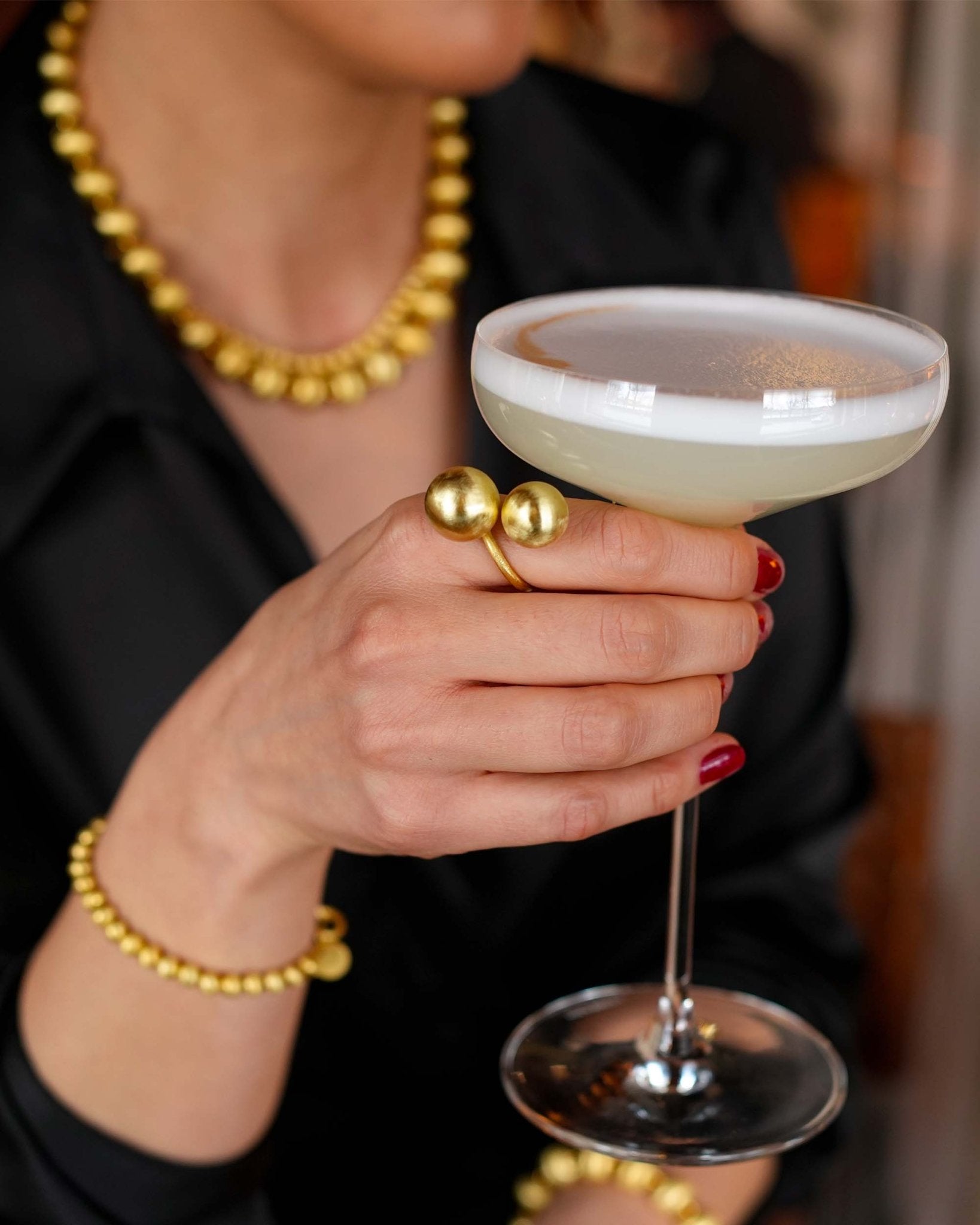 Hand mit Lumina Double Sphere Goldring hält ein Getränk – Lifestyle-Bild Cosytas
