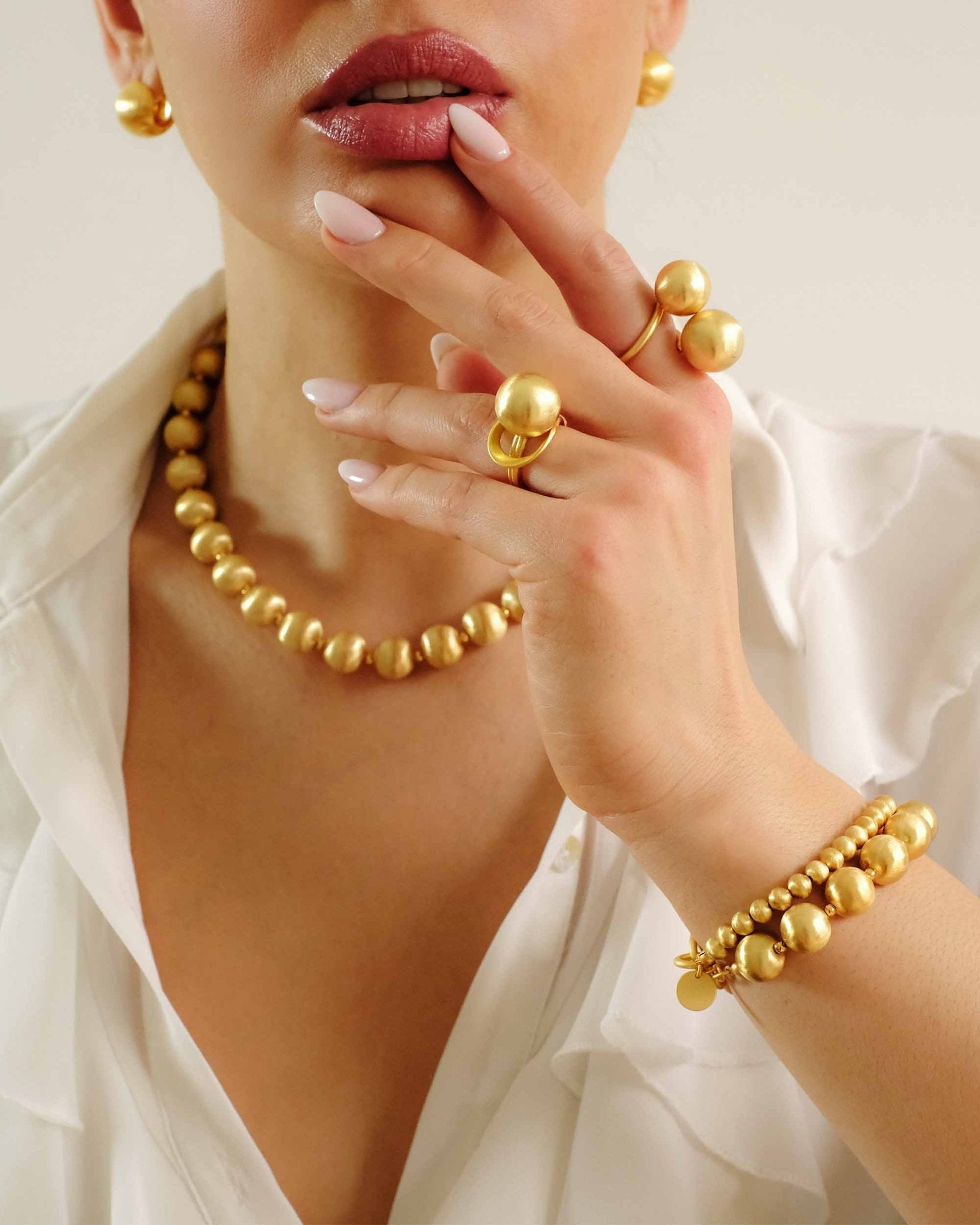 Frau mit Lumina Gold Kollektion: Kugelkette, Armband, Ring und Ohrringe in 18K vergoldetem Metall