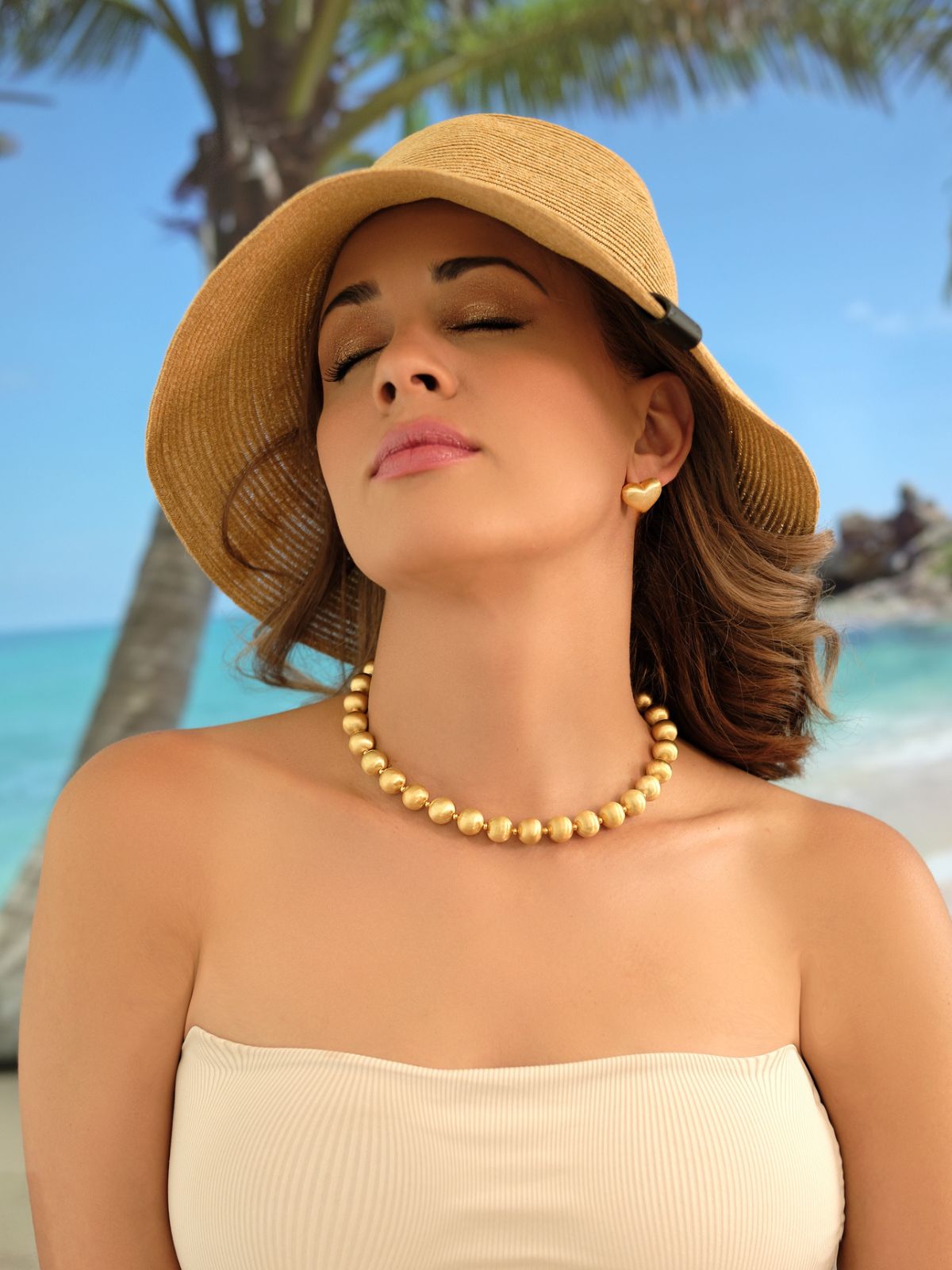 Frau mit Cosytas Statement-Halskette Lumina Bold Gold am Strand unter Palmen