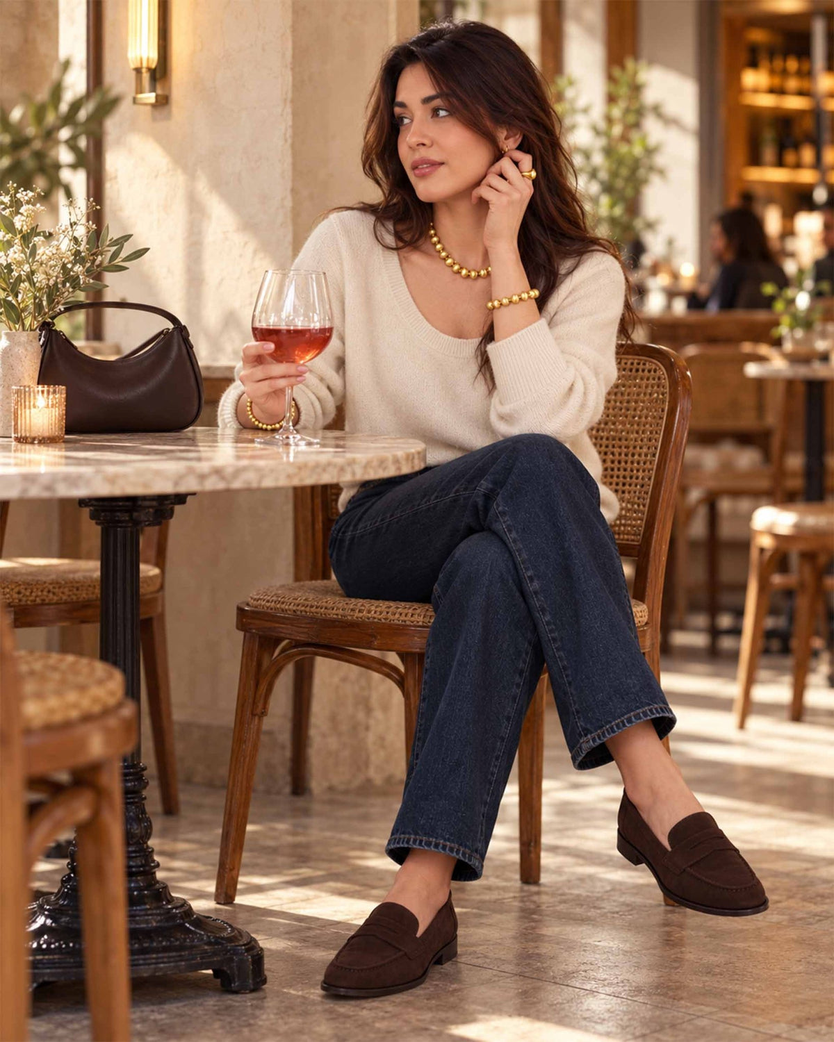 Mujer con jersey color crema, vaqueros oscuros y mocasines marrones que lleva el collar, la pulsera, los pendientes y el anillo Lumina Gold