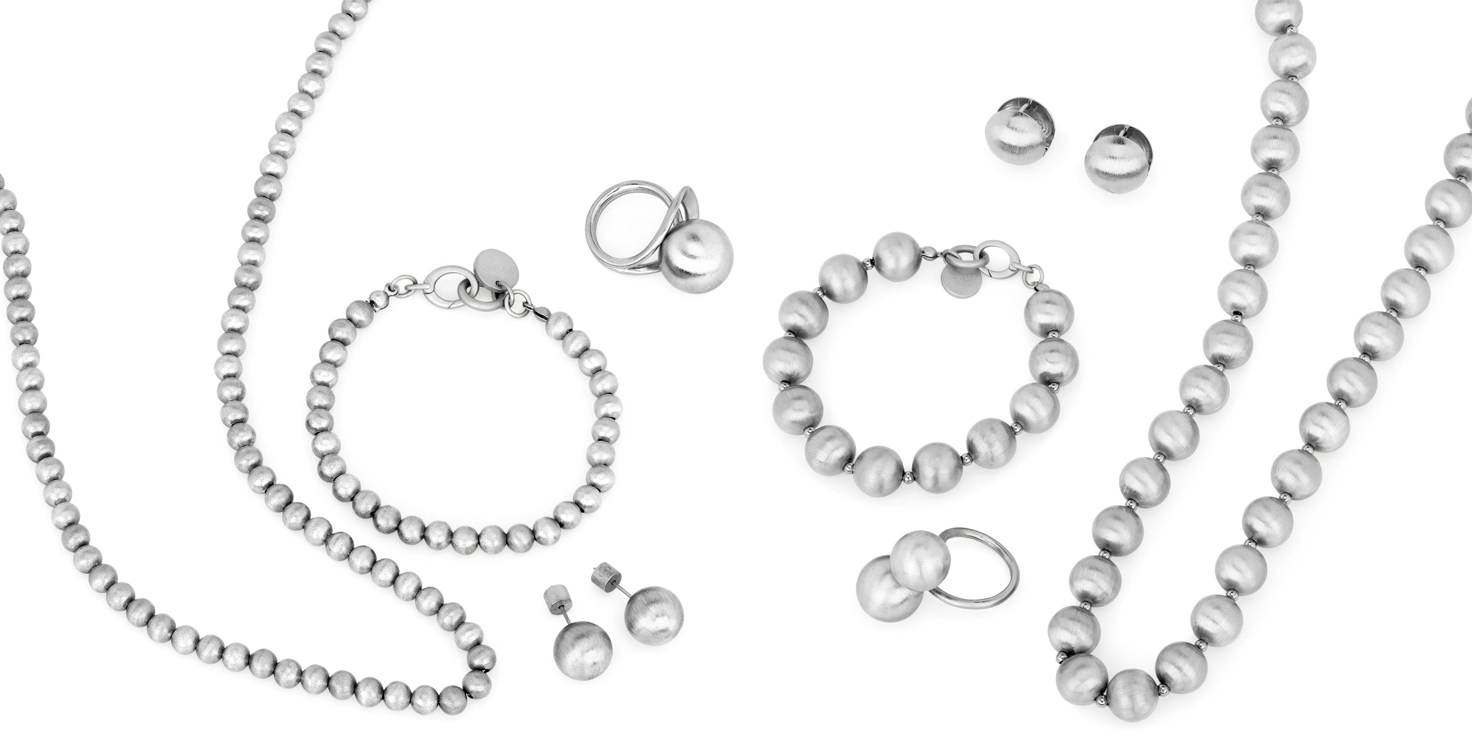 Flach gelegte Schmuckkollektion in Silber bestehend aus Halsketten, Armbändern, Ringen und Ohrringen mit Kugel- und Perlendetails, elegant arrangiert auf weissem Hintergrund.