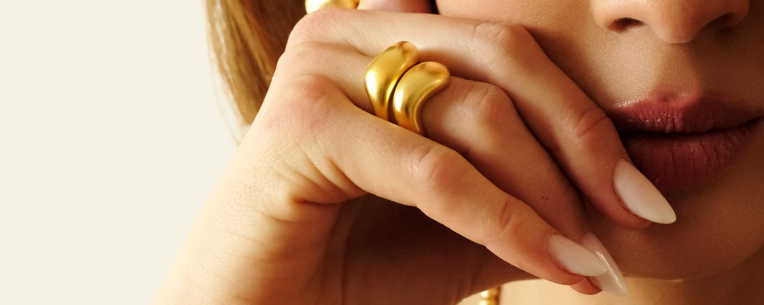 Nahaufnahme einer Hand mit eleganten goldenen Ringen. Die Ringe haben ein geschwungenes, modernes Design und ergänzen den stilvollen Look.