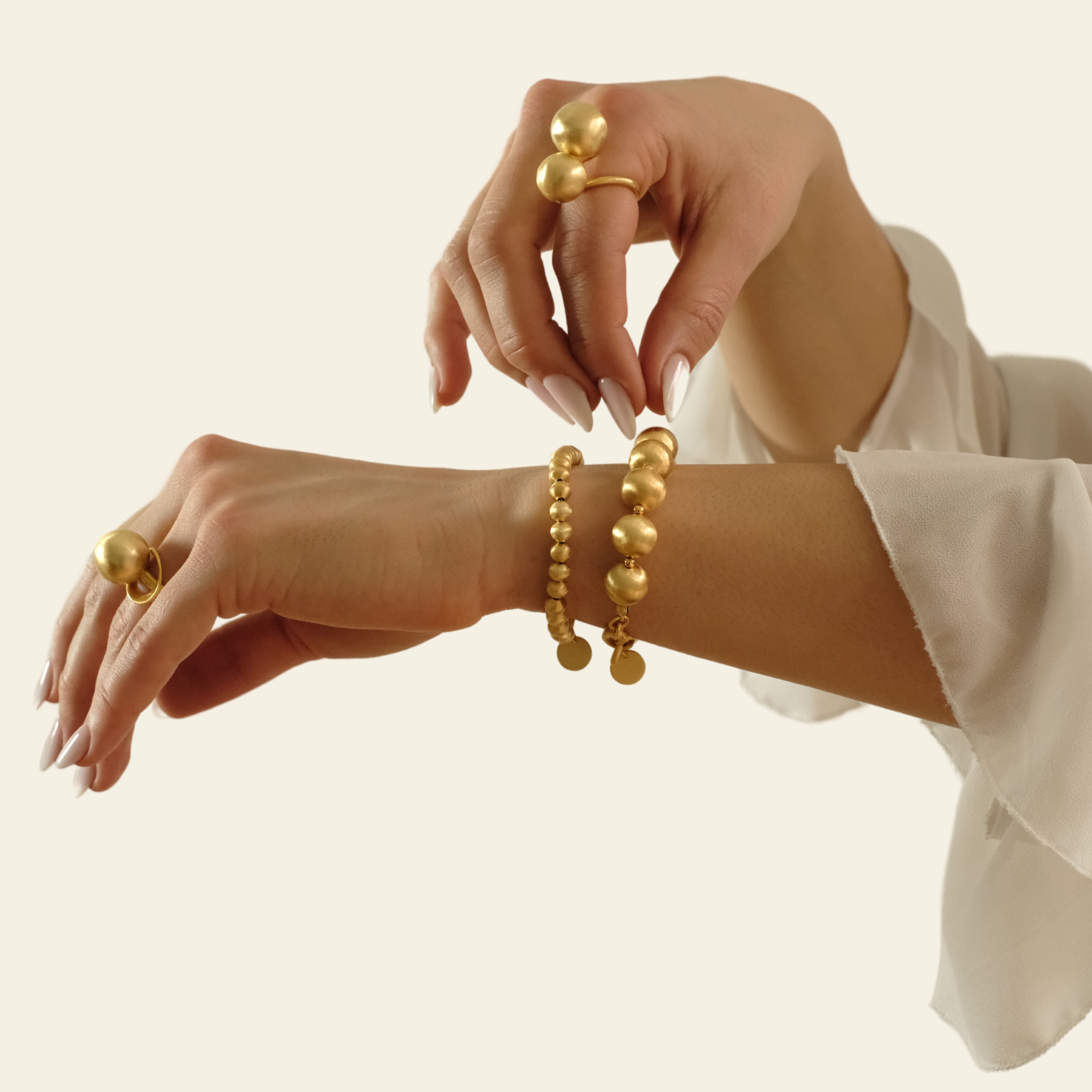 Cosytas Schmuck-Kombination aus goldenen Armbändern und auffälligen Statement-Ringen mit grossen, gebürsteten Kugelperlen, veredelt mit 18k Gold. Ideal für einen markanten und stilvollen Auftritt.