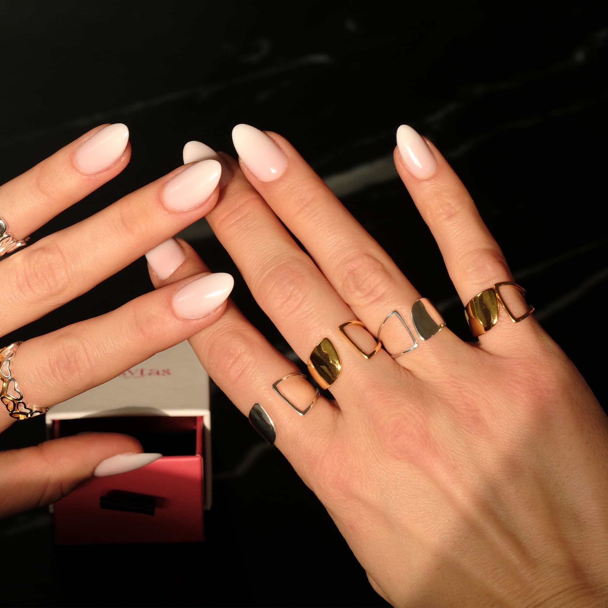Detailaufnahme von Händen mit dem Cosytas Arc Ring in Gold und Silber. Das geometrische Design der offenen Ringe kombiniert glänzende und matte Oberflächen für einen modernen, architektonischen Look. Im Hintergrund eine Cosytas-Schmuckbox.