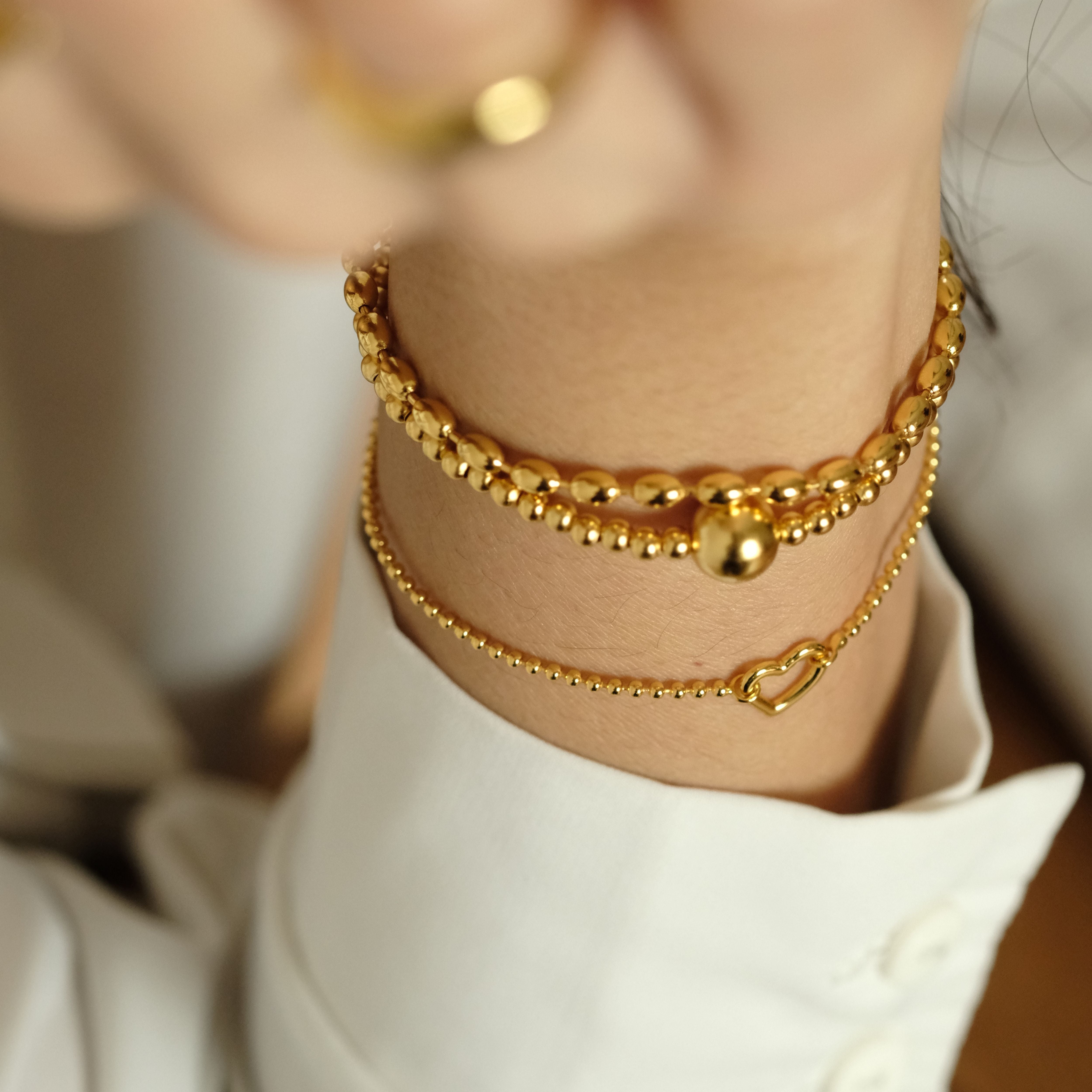 Goldene Armband-Kombination von Cosytas mit filigranen und kugelförmigen Designs, veredelt mit 18k Gold. Stilvolles Layering-Set für elegante und moderne Looks.