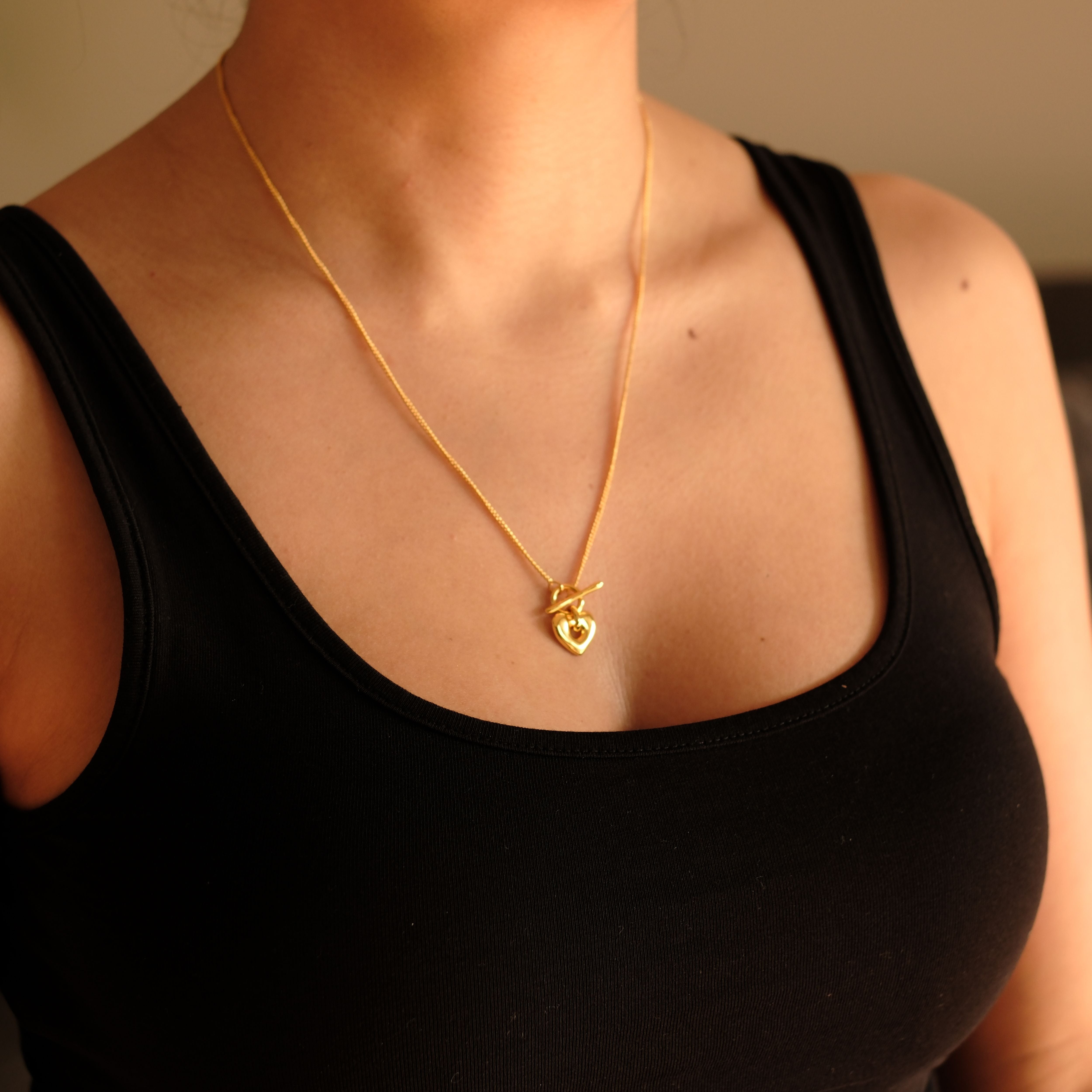 Cosytas goldene Halskette mit Herzanhänger und Knebelverschluss, gefertigt aus hochwertiger Metalllegierung und veredelt mit 18k Gold. Feminines und verspieltes Design als besonderer Blickfang.