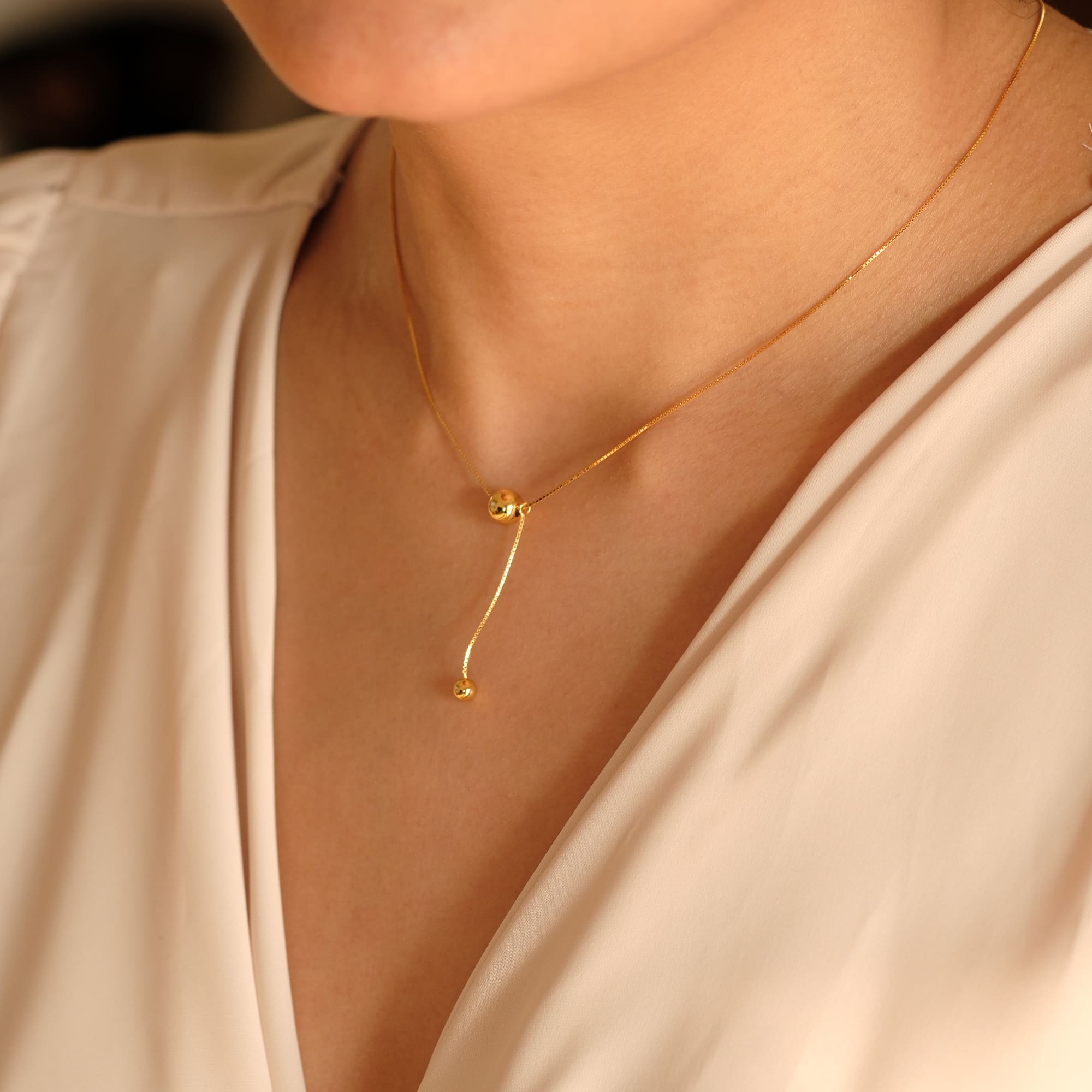 Model trägt die Cosytas Golden Balance Halskette. Feines Y-Design mit zwei polierten Kugeln für eine moderne, fliessende Silhouette. Die goldene Kette verleiht jedem Look Eleganz und Leichtigkeit.