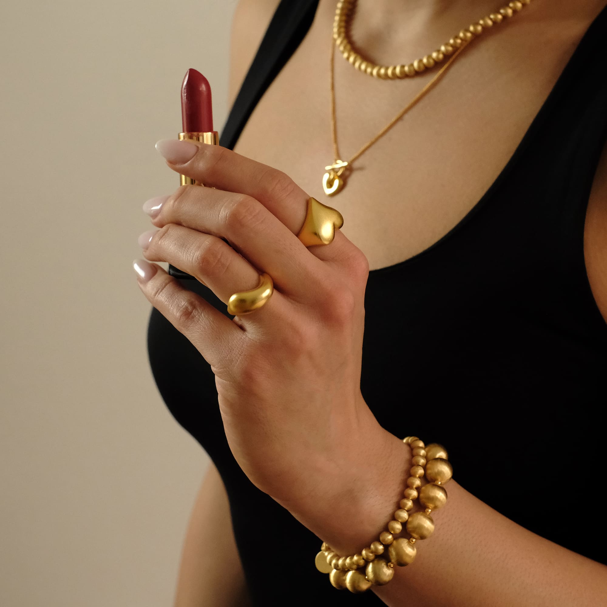 Stilvolle Hand mit dem Cosytas Golden Dune Ring, kombiniert mit weiteren goldenen Schmuckstücken. Die elegante Pose mit rotem Lippenstift unterstreicht den luxuriösen, modernen Look.