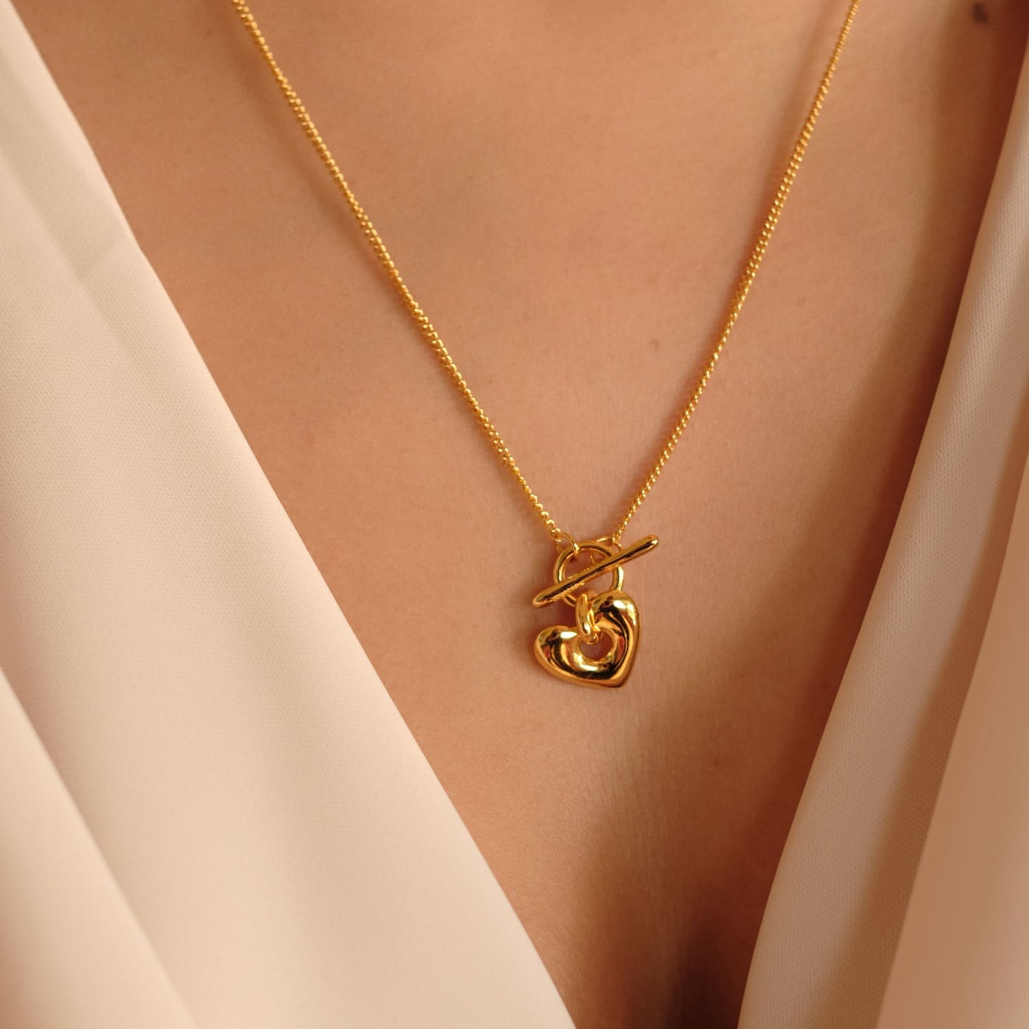 Nahaufnahme einer eleganten goldenen Halskette von Cosytas mit einem Herzanhänger, getragen über einem cremefarbenen Oberteil. Minimalistisches und stilvolles Design im Fokus.