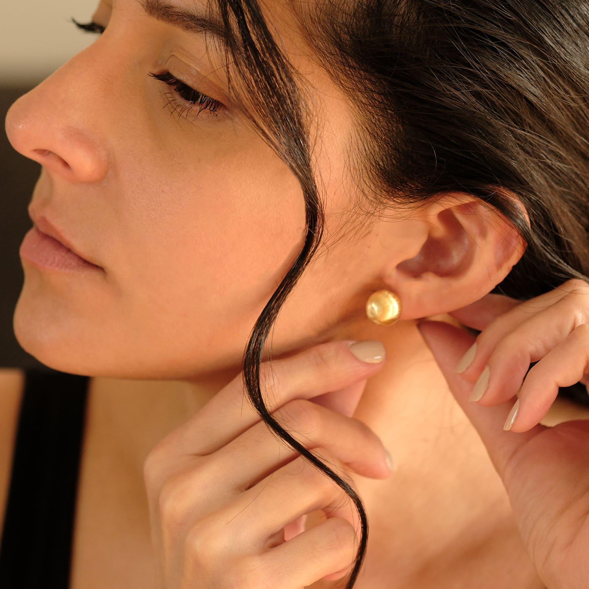 Nahaufnahme einer Frau mit den Cosytas Lumina Bold Gold Ohrringen. Die runden, goldplattierten Ohrstecker strahlen zeitlose Eleganz aus und setzen ein kraftvolles Statement.