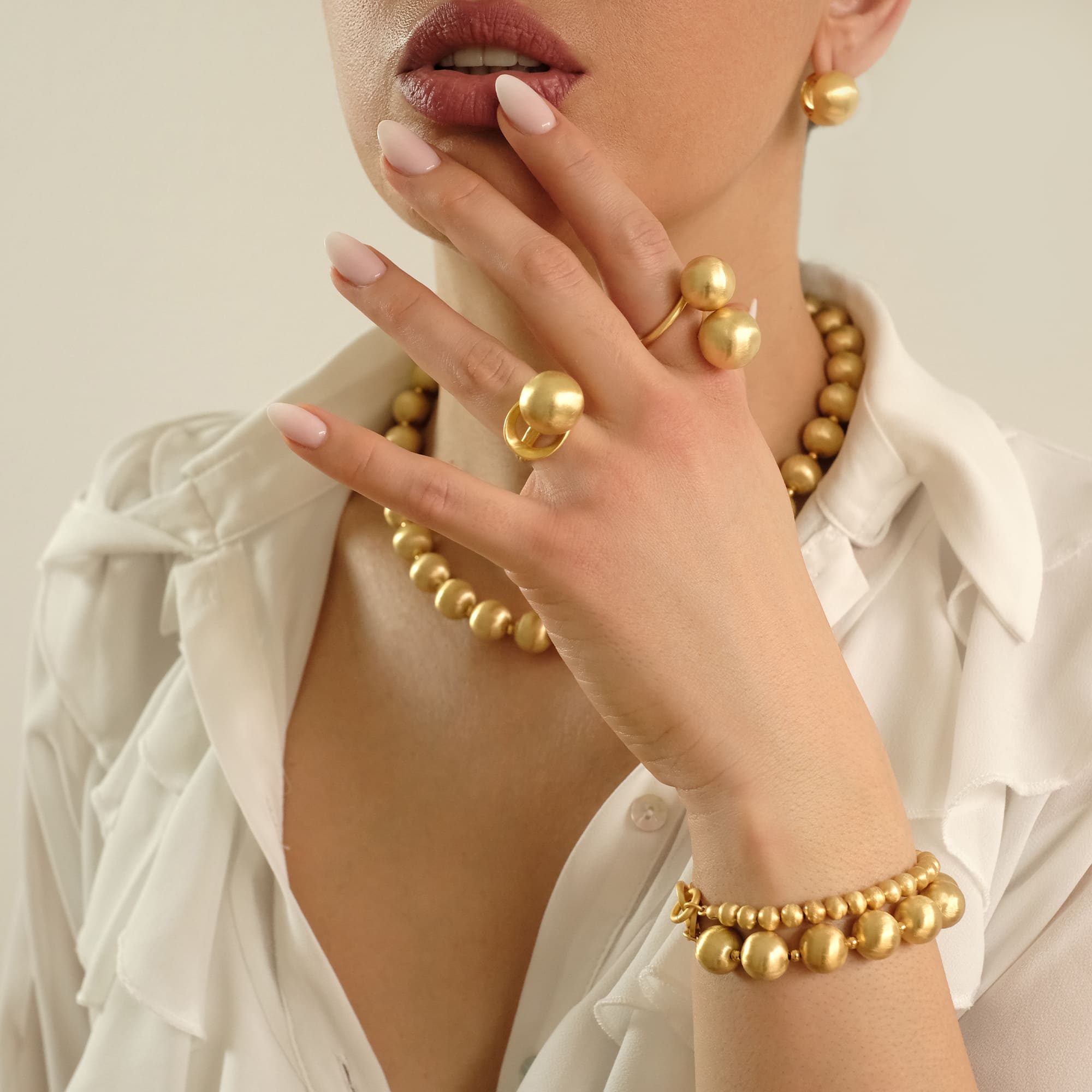 Model trägt das Cosytas Lumina Gold Schmuck-Set mit Kugel-Design. Elegante Halskette, Armband, Statement-Ringe und Ohrringe in warmem Goldton. Weiches Licht betont die edle Oberfläche und das luxuriöse Design.