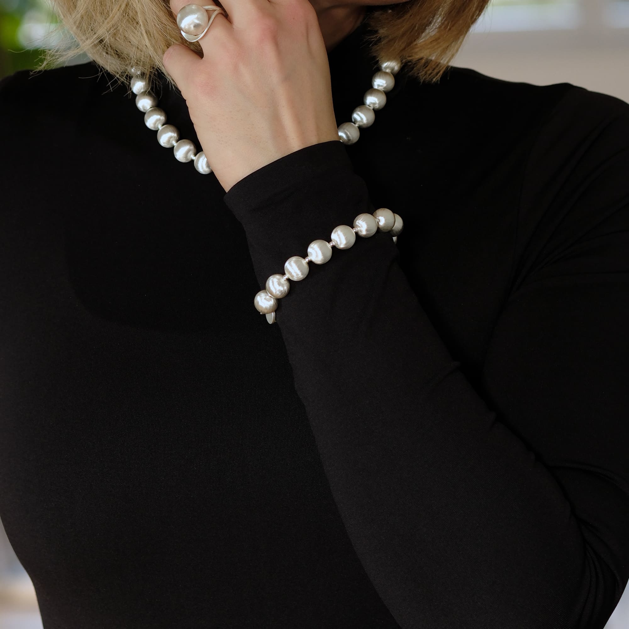 Model trägt das Cosytas Lumina Silver Sphere Armband und die passende Halskette mit silbernen Kugeln. Dezentes, elegantes Design, das zeitlosen Stil mit modernem Touch kombiniert. Perfekt für raffinierte Looks.