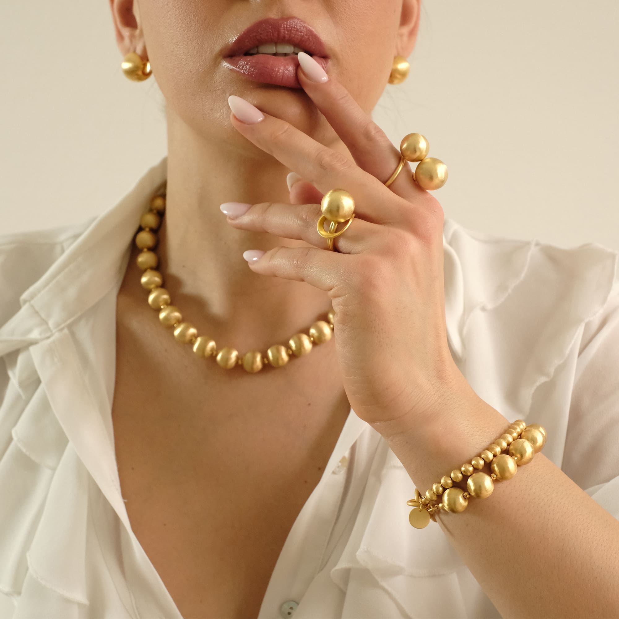 Model trägt das Cosytas Lumina Gold Schmuck-Set mit Kugel-Design. Elegante Halskette, Armband, Statement-Ringe und Ohrringe in warmem Goldton. Weiches Licht betont die edle Oberfläche und das luxuriöse Design.