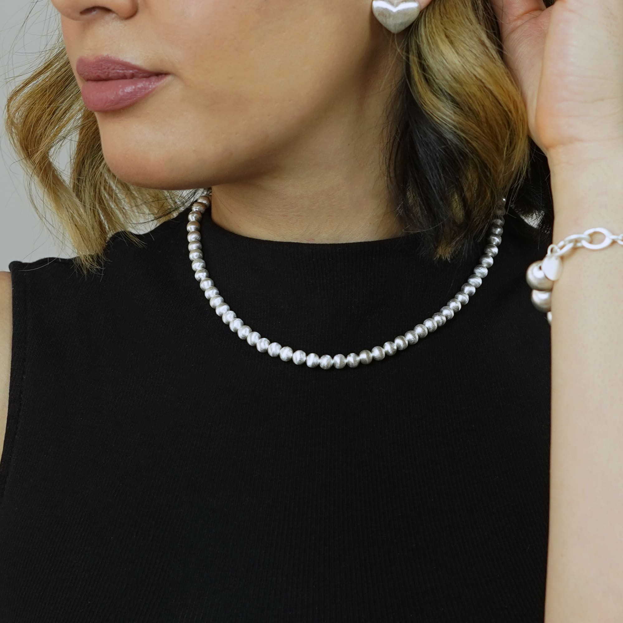 Model trägt die Cosytas Lumina Slim Silver Sphere Halskette. Feine, silberne Kugelkette mit dezenter Eleganz, kombiniert mit passendem Armband und herzförmigen Ohrringen. Zeitloses Design für stilvolle Looks.