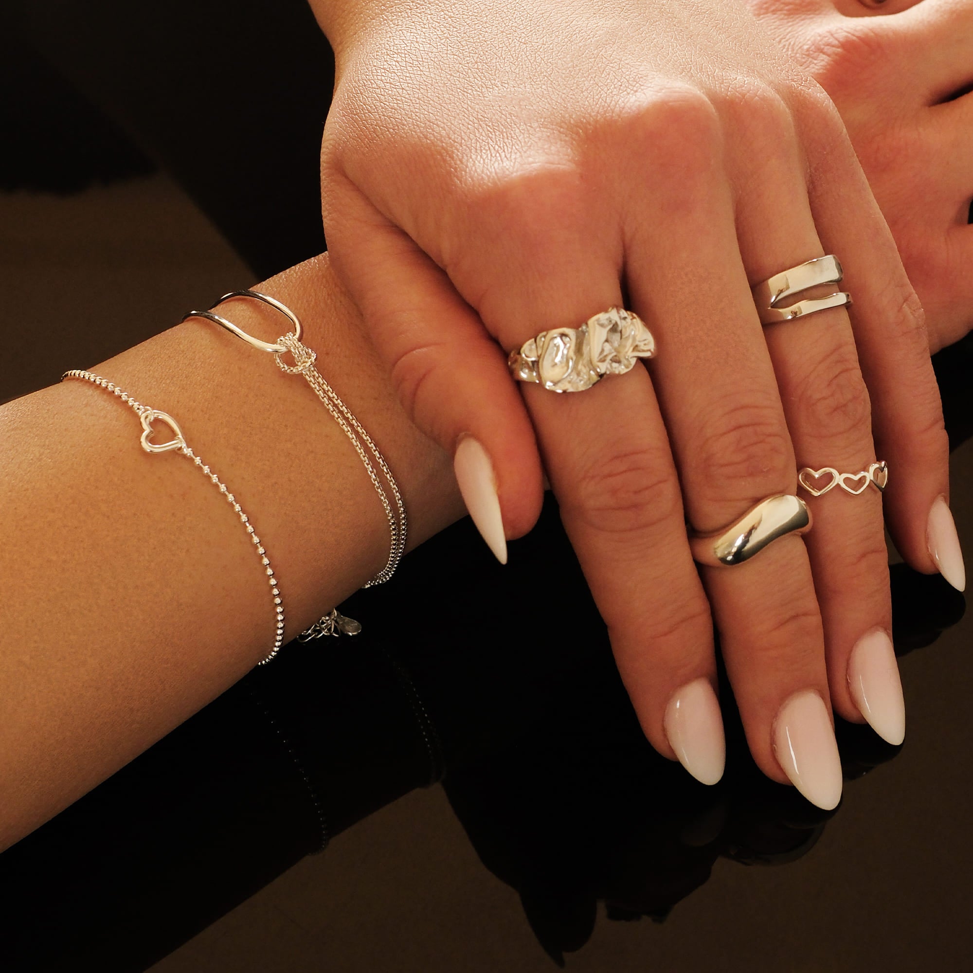 Model trägt das Cosytas Silver Harmony Armband. Feine, silberne Armbänder mit filigranen Herz- und Ringdetails, kombiniert mit modernen Statement-Ringen für einen eleganten und romantischen Look.