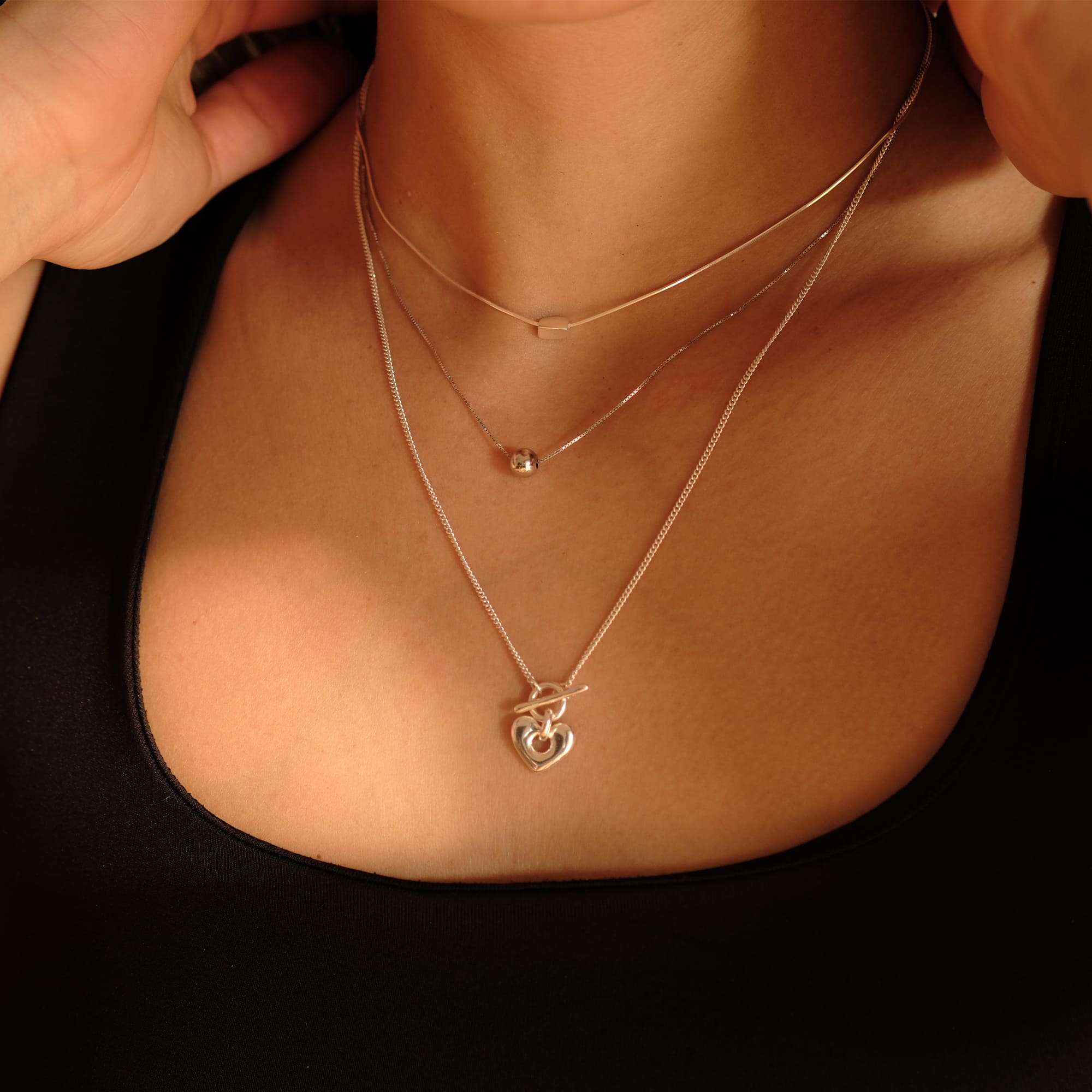 Model trägt die Cosytas Silver Heartbeat Halskette im Layering-Stil mit zwei weiteren feinen Silberketten. Der Herzanhänger mit elegantem Verschluss setzt einen romantischen Akzent für einen modernen, stilvollen Look.