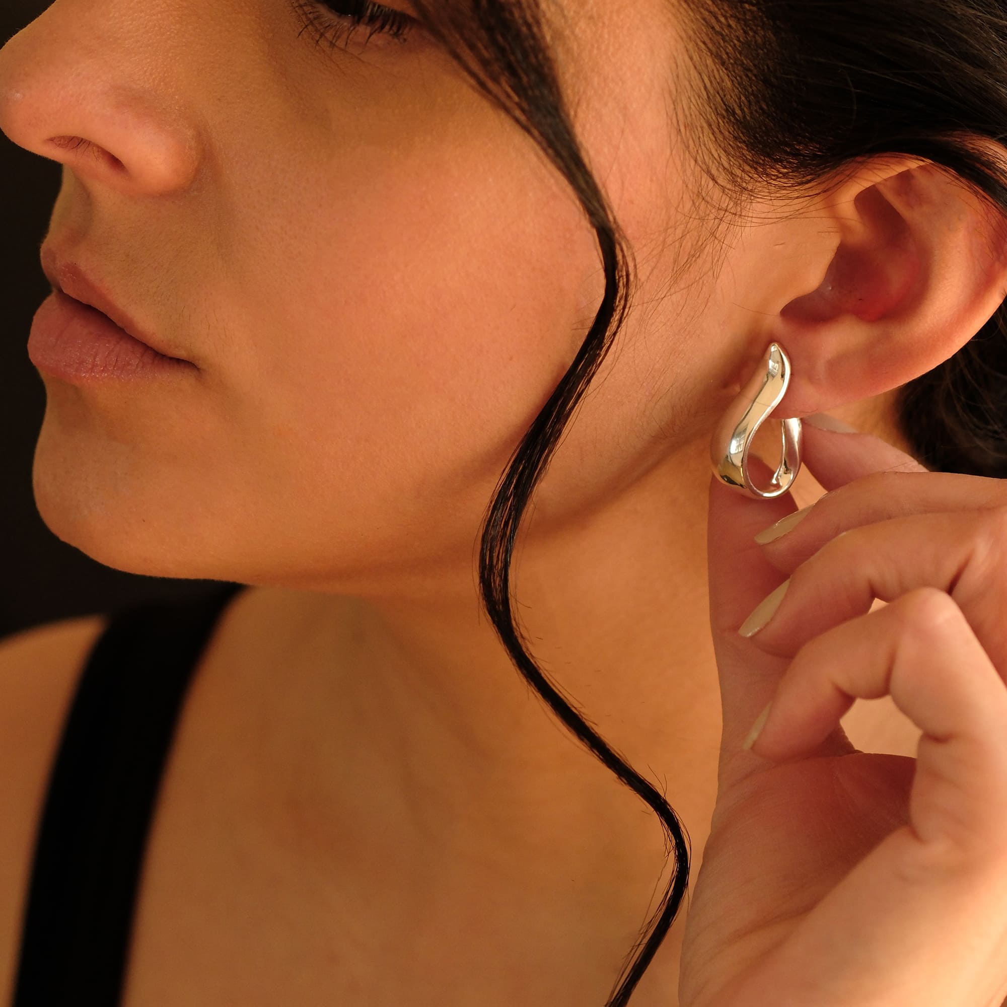 Nahaufnahme einer Frau mit den Cosytas Silver Wave Hoops. Die geschwungenen Creolen aus glänzendem Silber vereinen moderne Eleganz mit einer organischen, fliessenden Form.