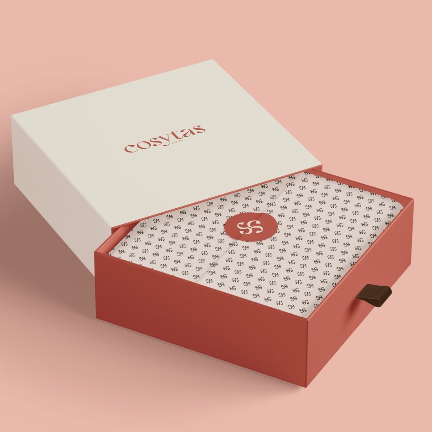 Stilvolle geöffnete Geschenkbox von Cosytas in warmen Farben mit Logo und elegantem Verpackungsdesign auf einem rosa Hintergrund.