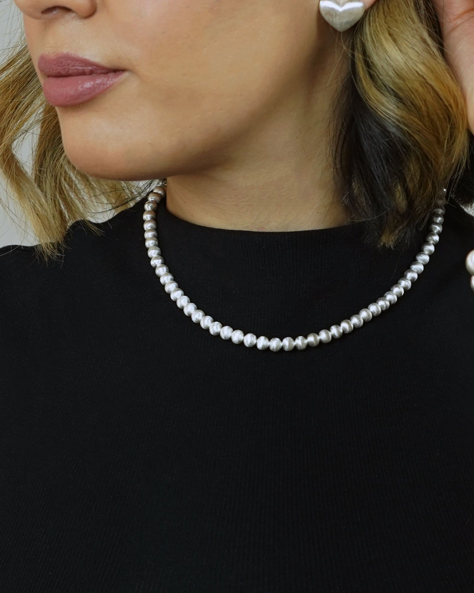 Model mit Cosytas Lumina Slim Silver Sphere Halskette, Armband und herzförmigen Ohrringen in Silber